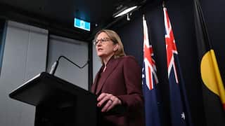 Jacinta Allan in a burgundy suit gives a speech at a lecturn with two Australian flags and one First Nations fla in the background