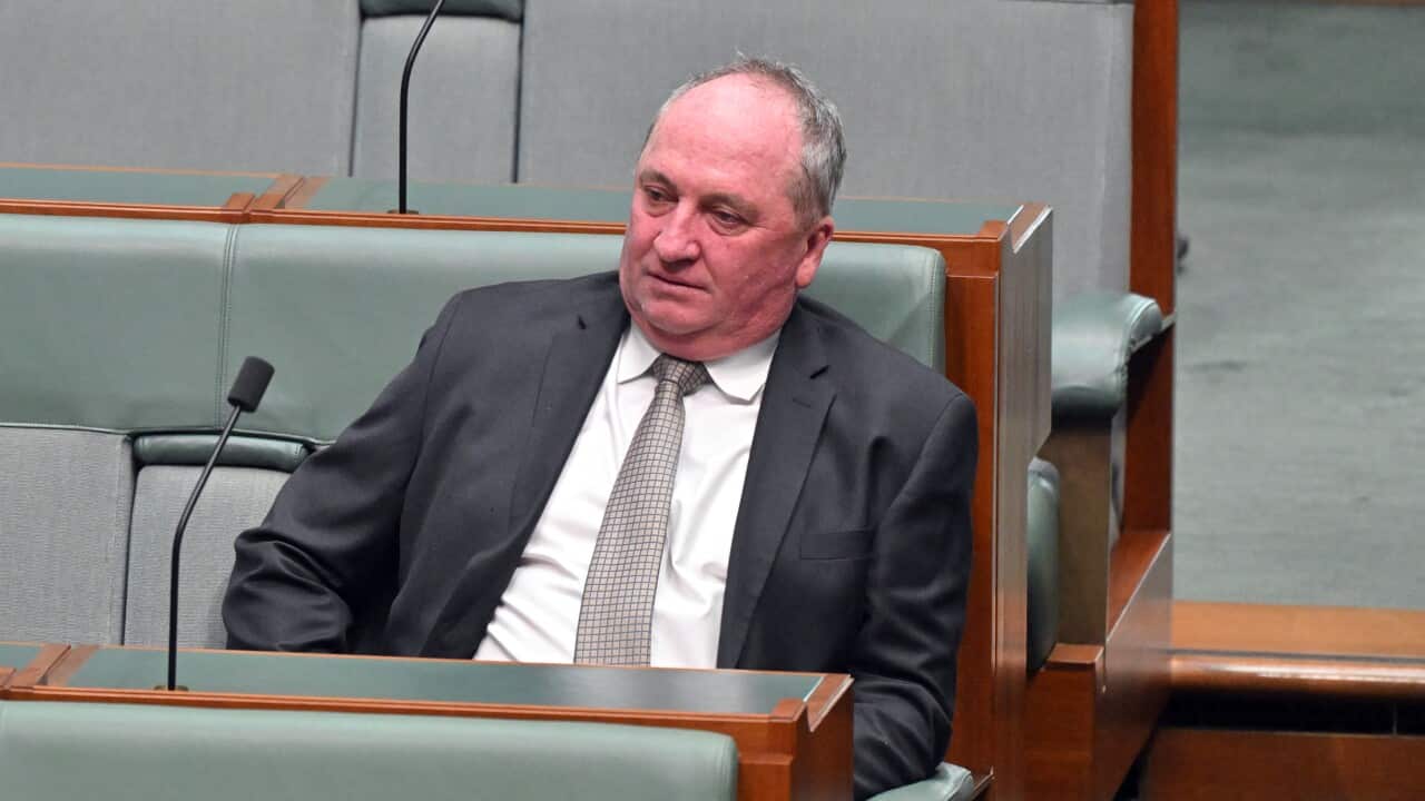 A man in a dark suit and tie sits looking downcast in a padded bench seat within Australia's House of Representatives.