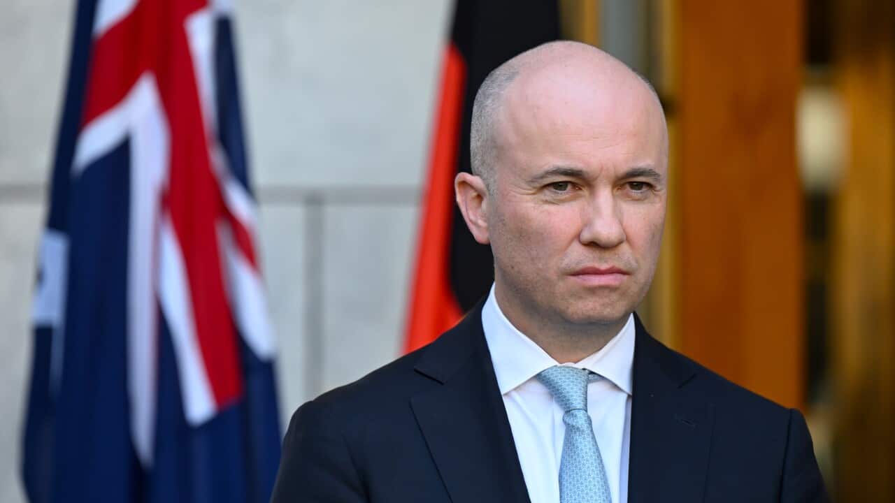 A man standing in front of Australian and Aboriginal flags.