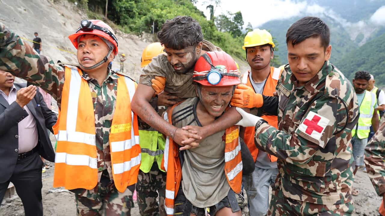 A rescue worker carries a person on his back, with two people in military uniform beside him.