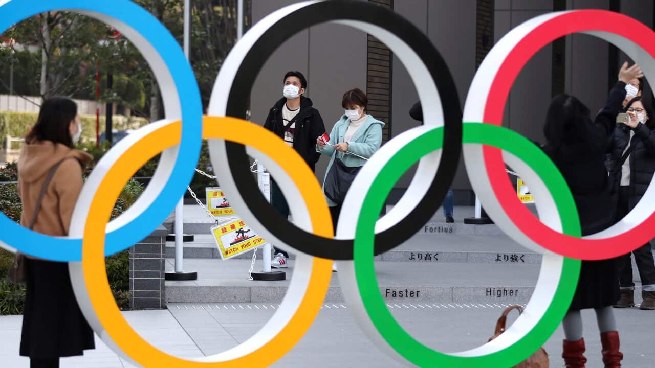 People wearing face masks walk by an Olympic rings installation at Japan Sport Olympic Square in Shinjuku, Tokyo.