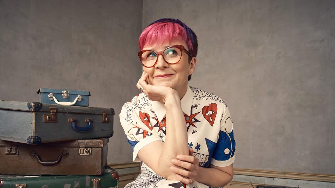 A woman sits smiling next to a stack of old suitcases.jpg