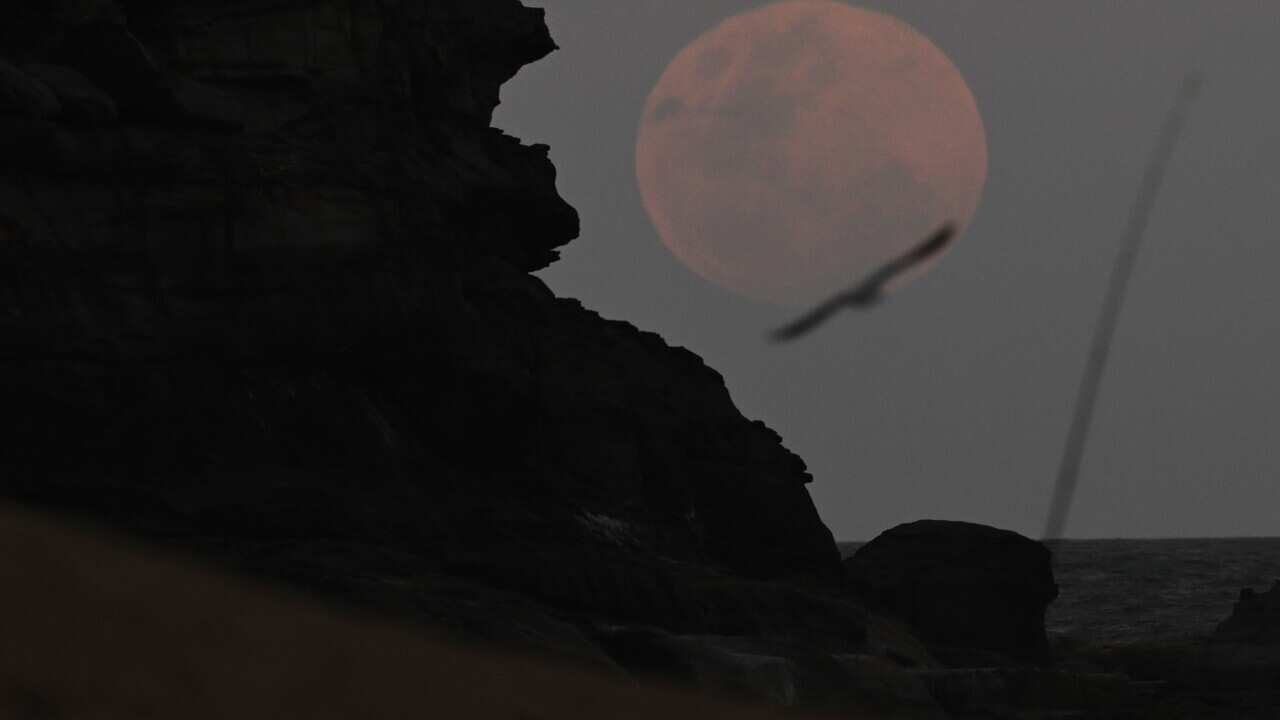 A full moon with a red hue. There is a cliff in the foreground