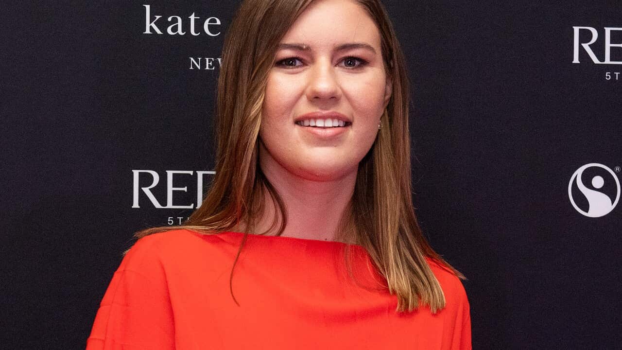 Brittany Higgins stands in front of a backdrop wearing a bright red-orange dress.