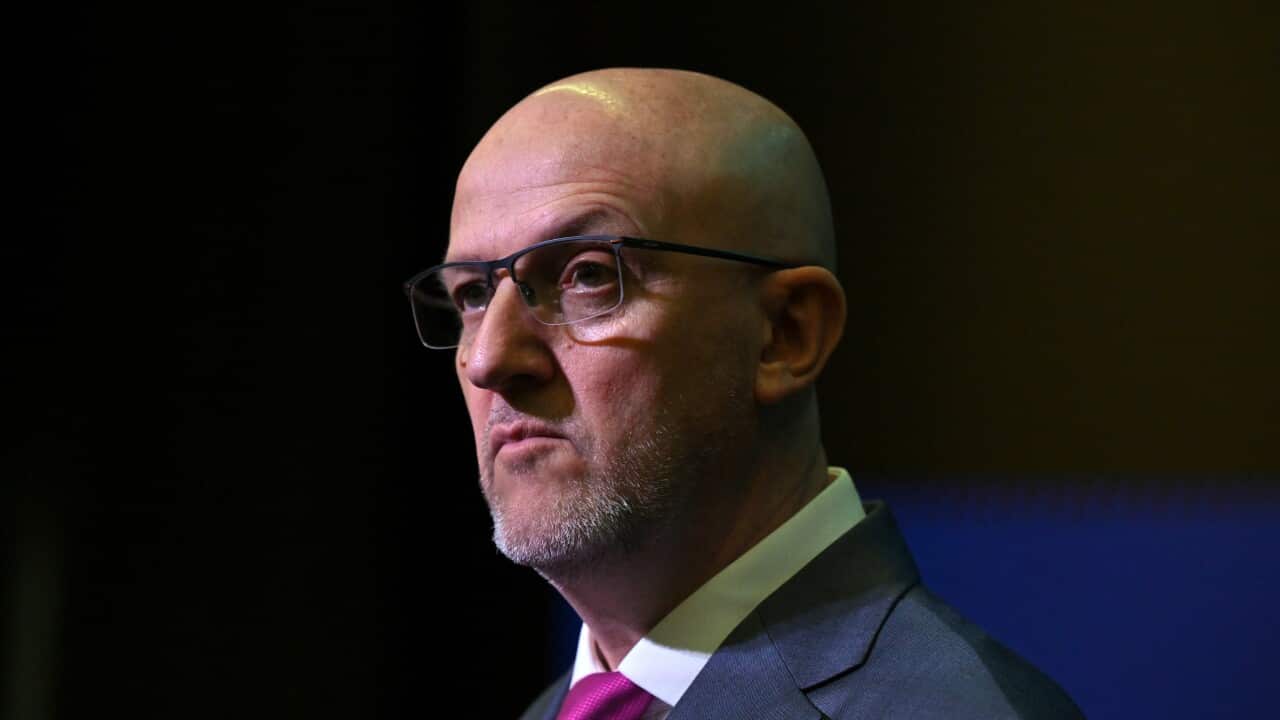 A man with a bald head wearing glasses, looking serious.