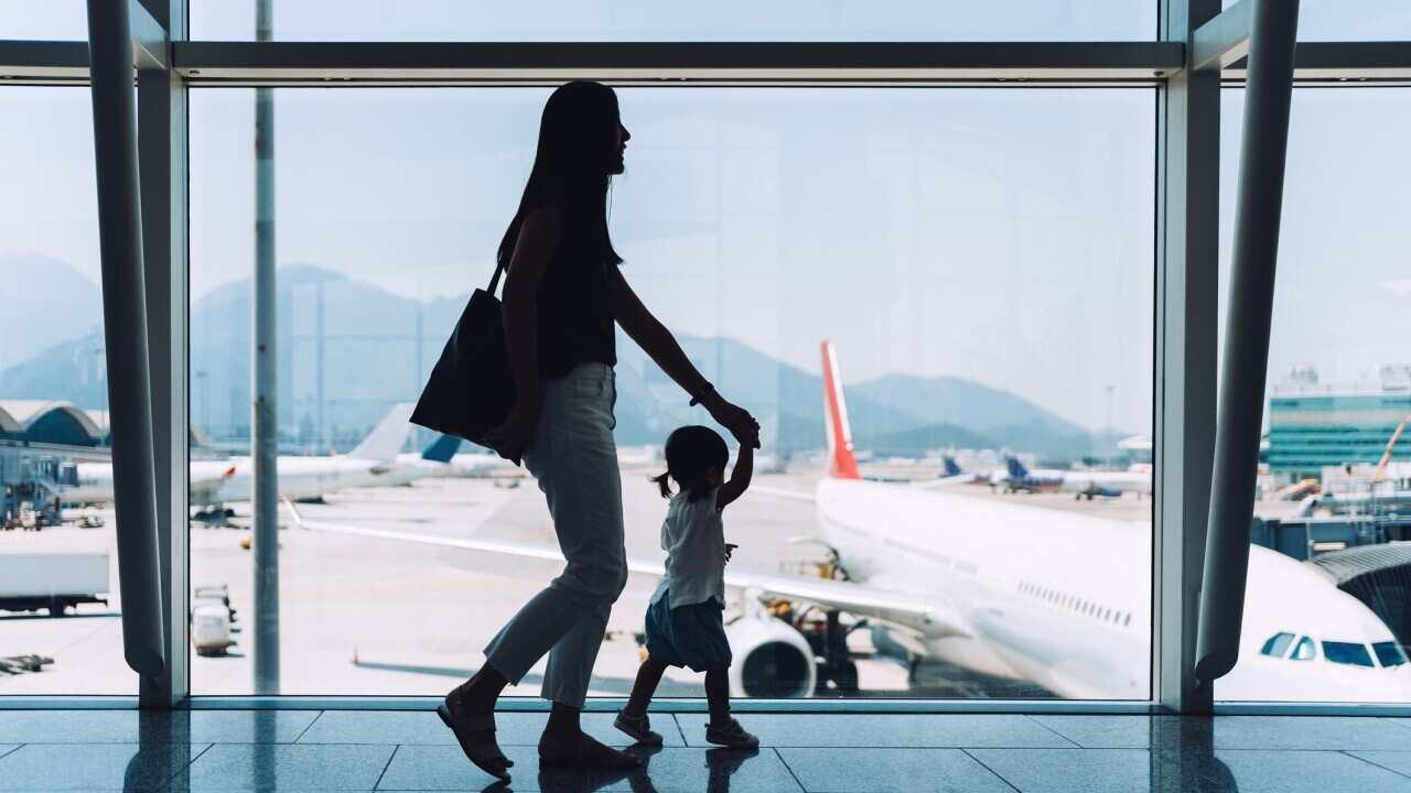 Silhouette of joyful young Asian mother holding hands of cute little daughter looking at airplane through window at the airport while waiting for departure