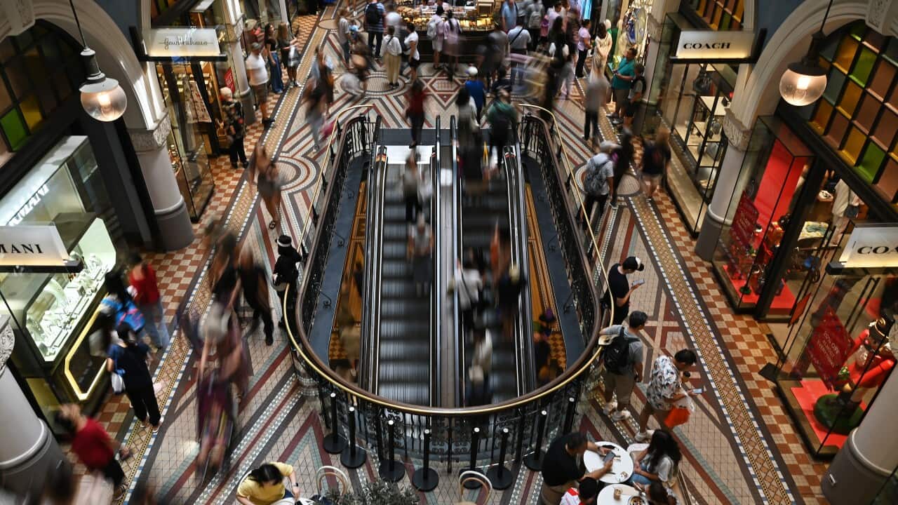 Busy shopping arcade with escalators and shoppers.