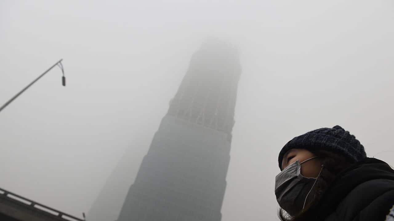 A woman waits for a bus below a skyscraper shrouded in smog on a heavily polluted day in Beijing on December 1, 2015. (GREG BAKER/AFP/Getty Images)