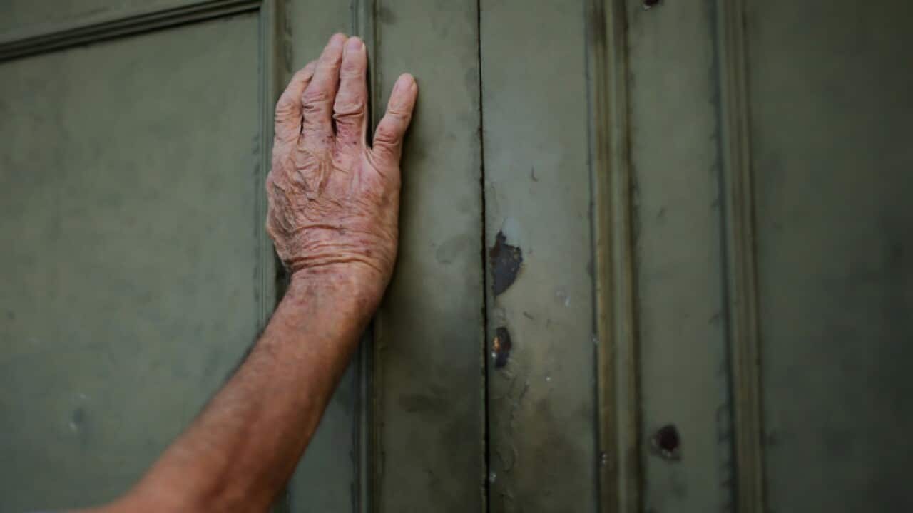 A senior citizen leans against a closed door