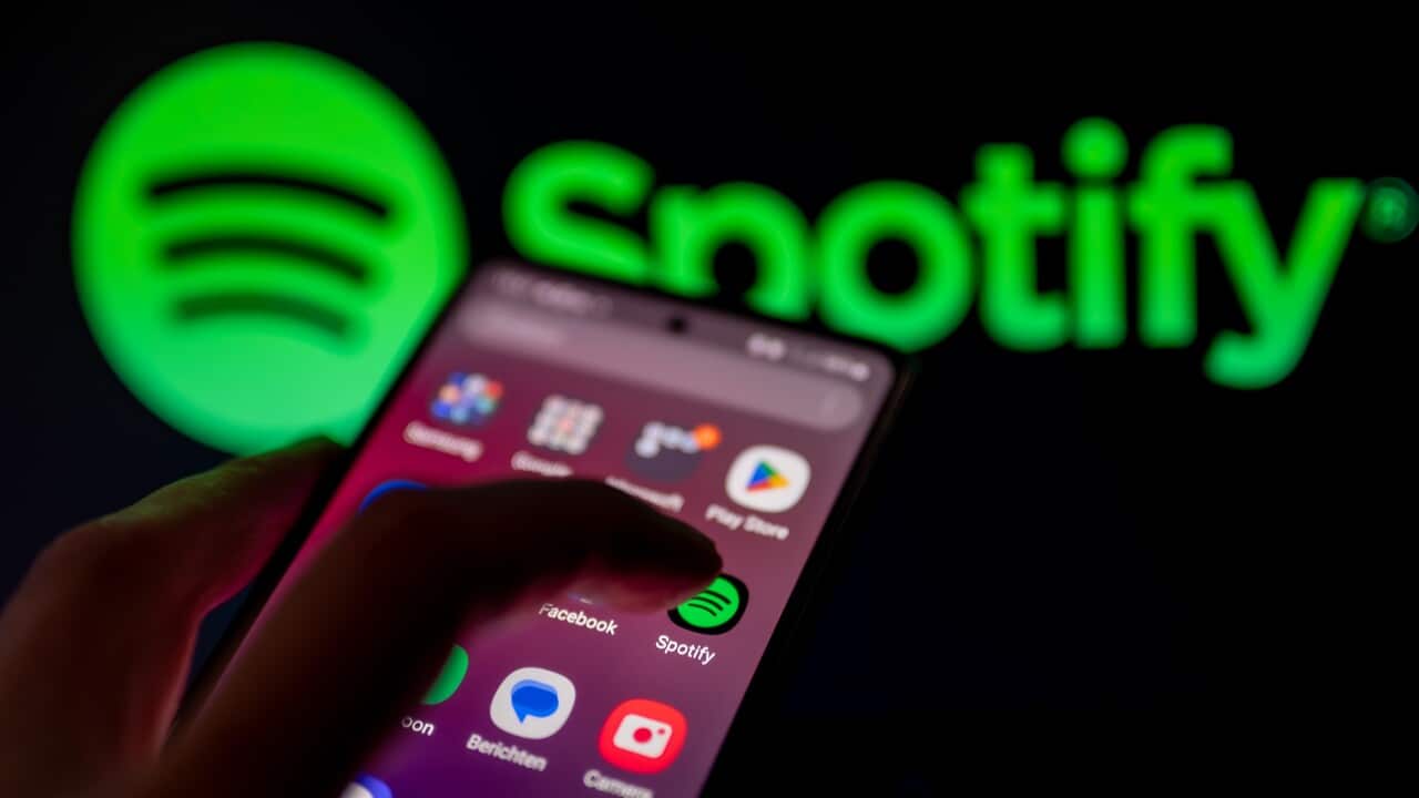 Finger tapping on Spotify app on smartphone. In the background is the Spotify logo