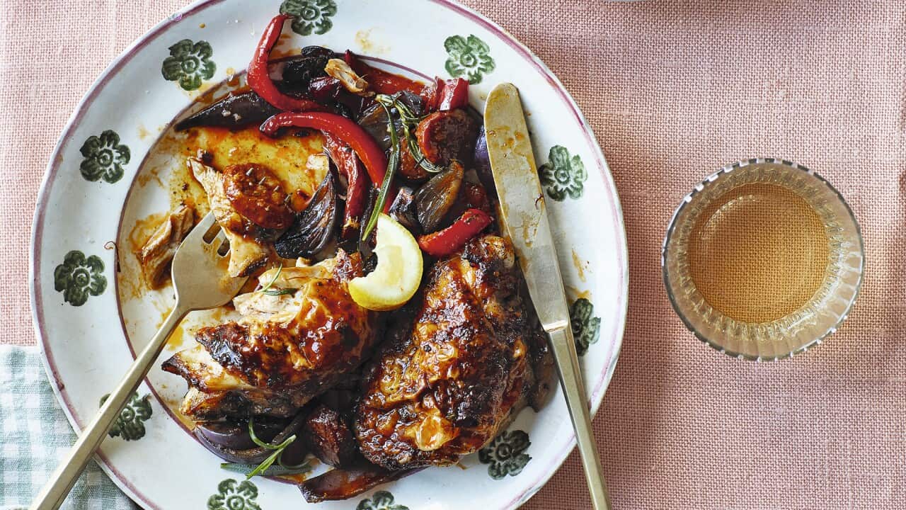 Two plates, holding serves of a chicken and capsicum dish, sit on a pale pink tablecloth. A folded napkin sits beside one plate.