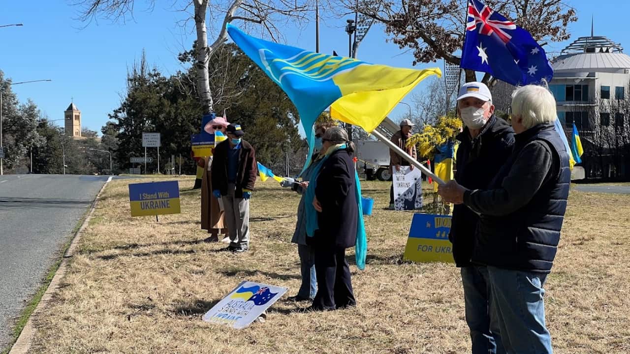 Ukrainians carry signs and Ukraine flags on the side of the road