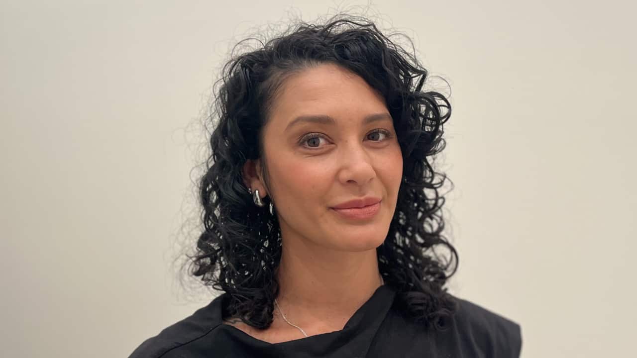 a closeup of a young woman with curly black hair in front of a white background