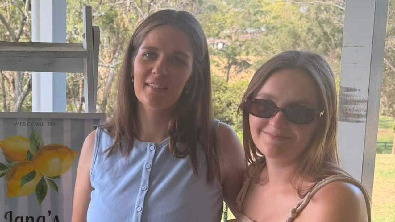 Two women stand together smiling on a covered veranda, next to a welcome sign featuring a lemon illustration that reads "Jana's Baby Shower."