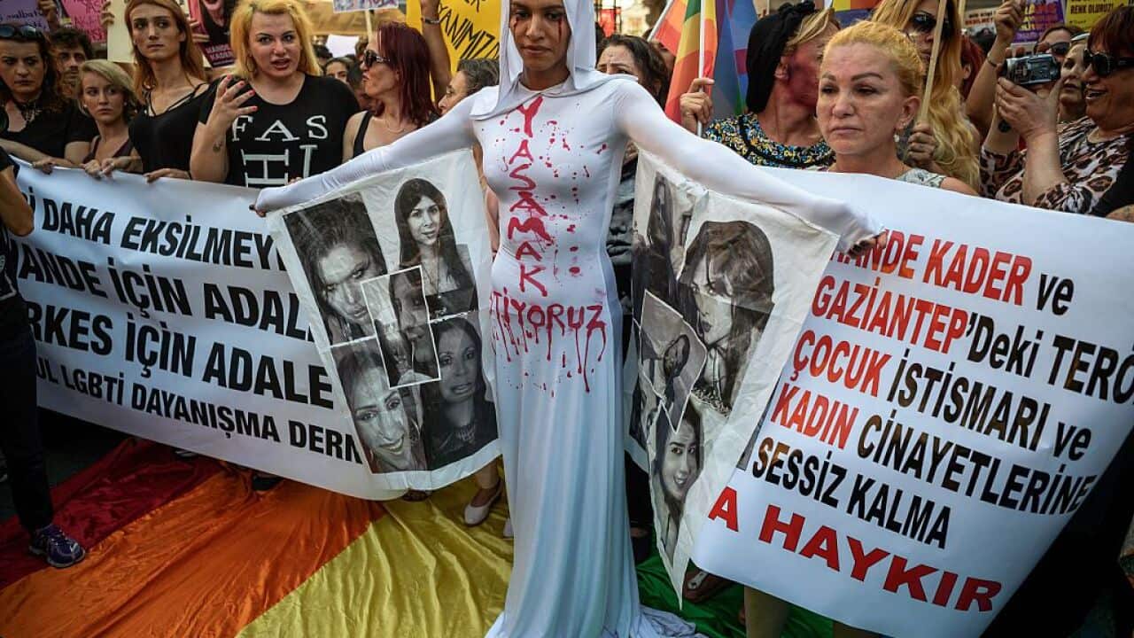 A LGBT member stands in front of a banner with make up on her face and a writing on her body "I want to live".