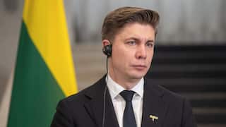 Lithuanian Prime Minister Mindaugas Sinkevicius with an earpiece in front of a Lithuanian flag.