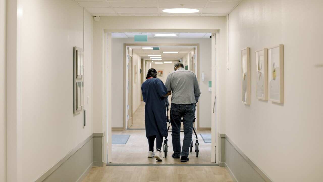 Rear view of female nurse walking with senior man at nursing home
