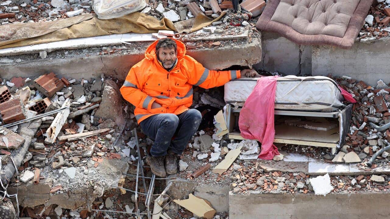 A man sitting holding the hand of someone who is beneath rubble.