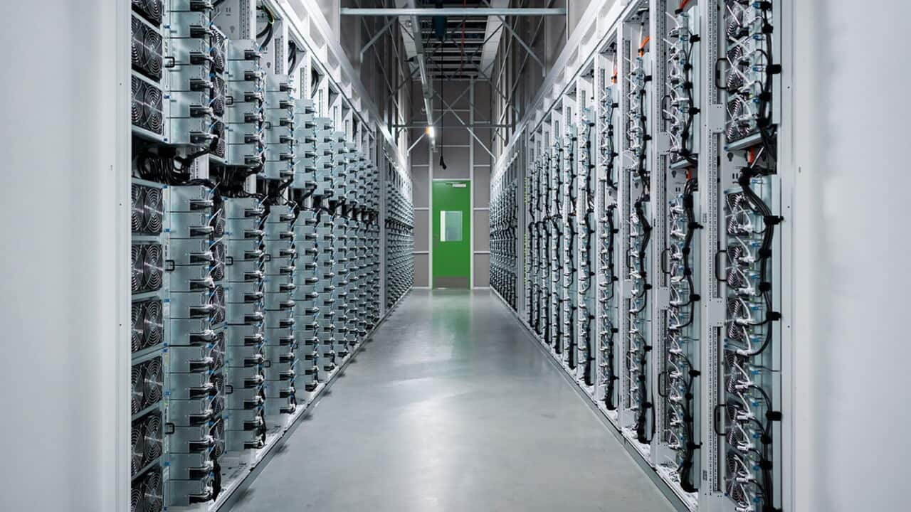 A long grey hallway filled with interconnected computer equipment leads to a green exit door.