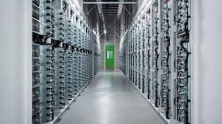 A long grey hallway filled with interconnected computer equipment leads to a green exit door.