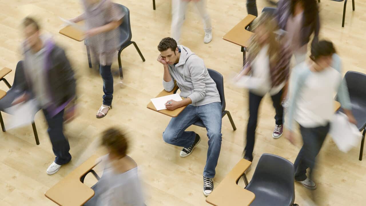 College students moving around man at desk in classroom
