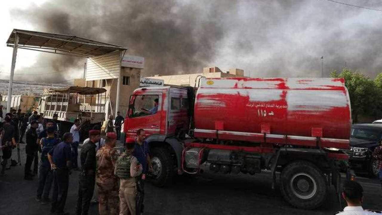 Iraqi security forces and firemen gather as smoke rises from a fire that broke out at Baghdad's largest ballot box storage site