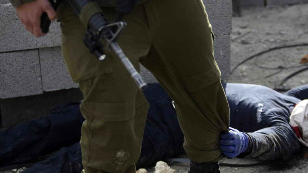 An injured settler grabs an Israeli soldier's leg