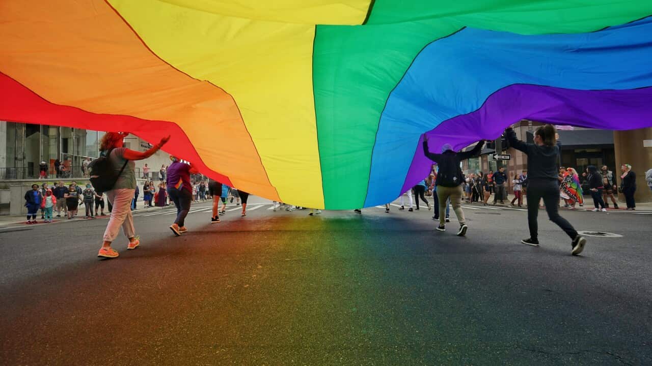 People Holding Large Colorful Flag While Walking On City Street