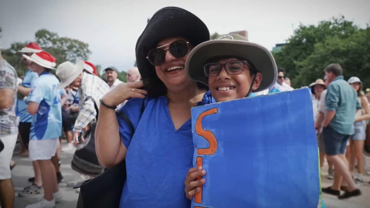 A woman and a young boy, both wearing broad-brimmed hats and glasses, smile as their photo is taken.