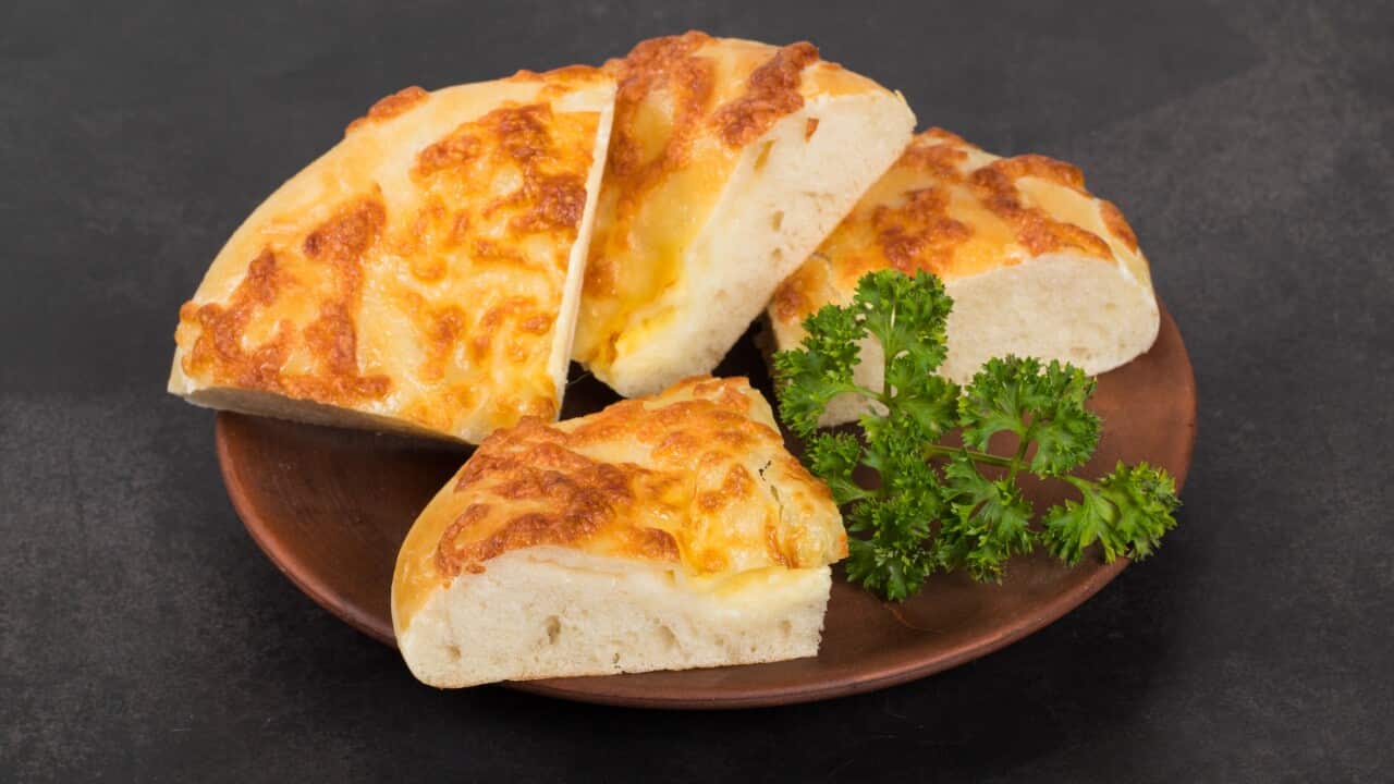 Sulguni cheese pie. With parsley. On a plate. Rustic style. Dark background. Close up