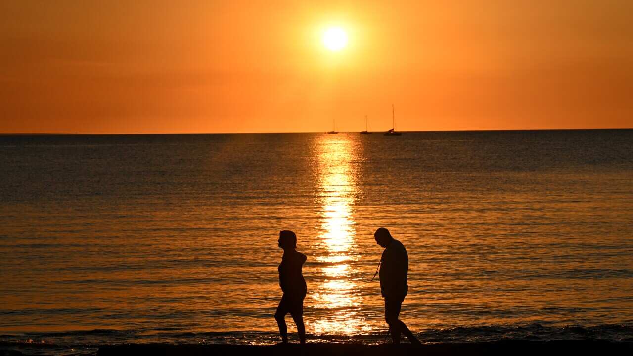 People are seen walking along Vesteys Beach as the sunsets in Darwin.