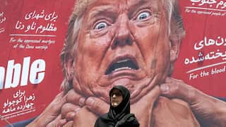 A woman in dark clothing and sunglasses passes a mural of a surprised old man with many hands around his neck.