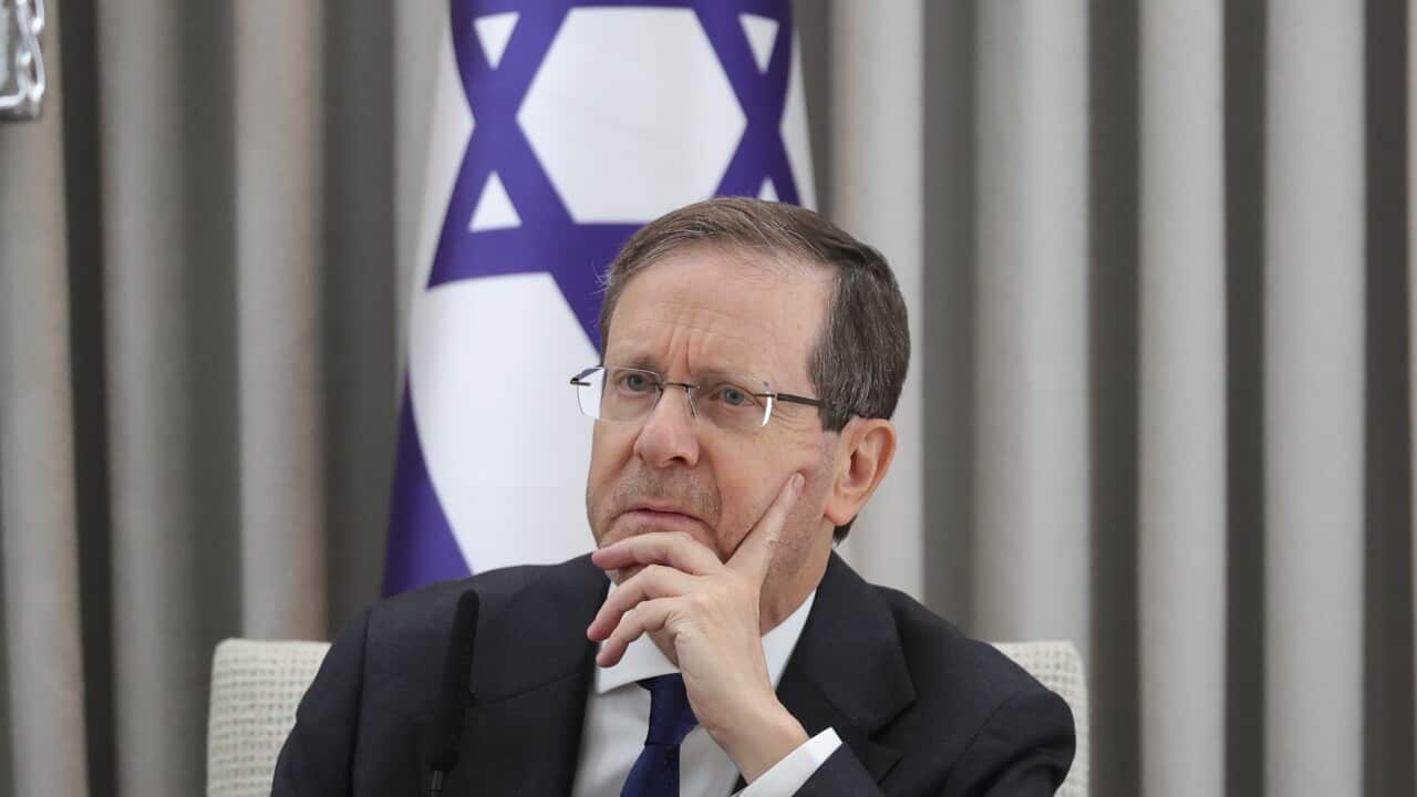 Isaac Herzog is sitting at a table with an Israeli flag behind him.