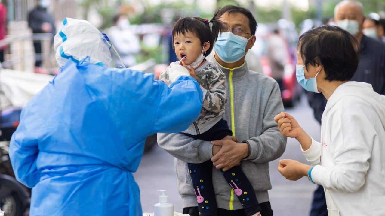 A healthcare worker collects a sample for a COVID-19 test from a child who is being held by a man.