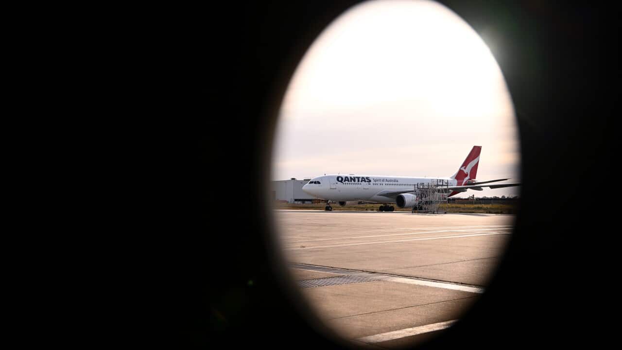 A Qantas aeroplane in focus on the tarmac, seen through a plane window, with a dark oval shaped shadow made by the window framing the scene.