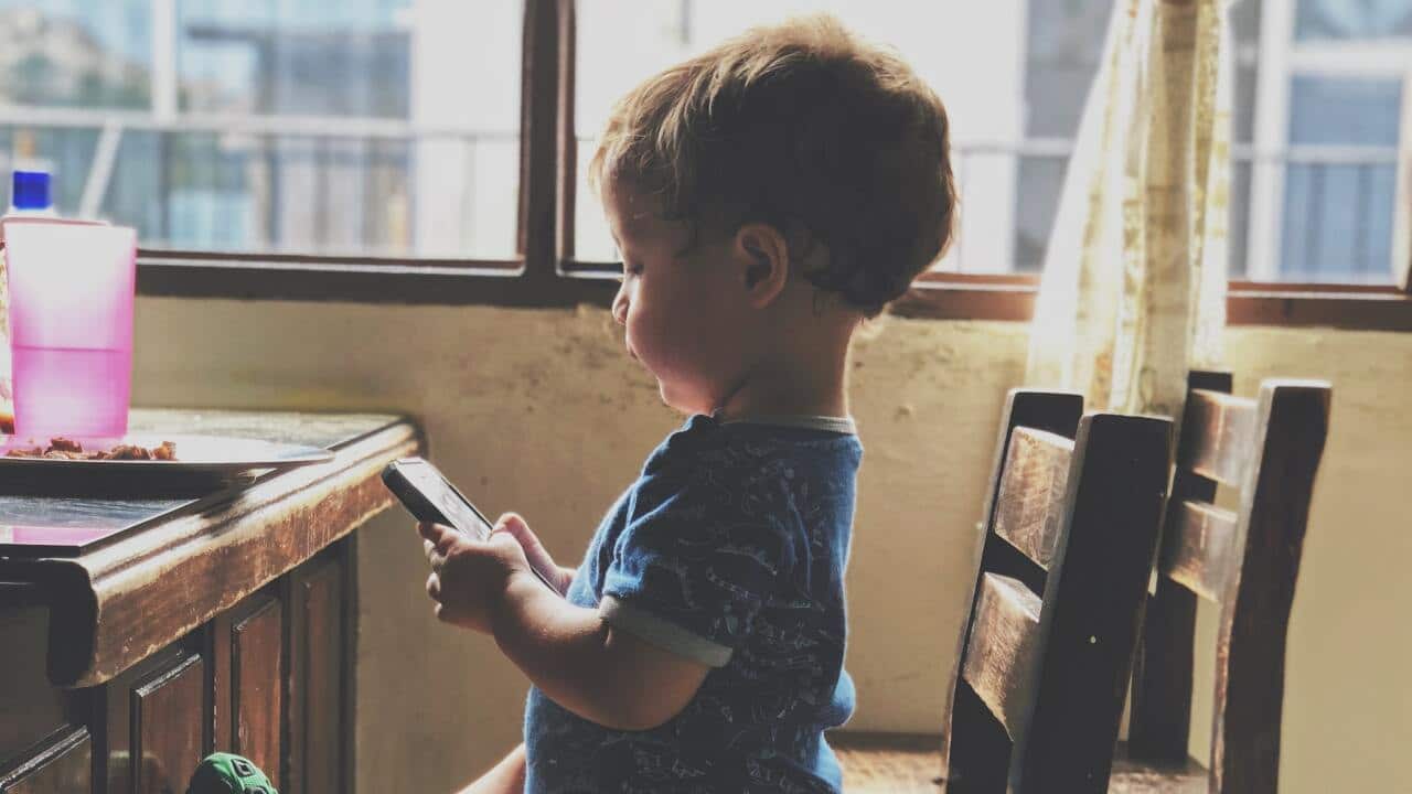 Umwana yicaye ku ntebe ariko arakinisha terefone.