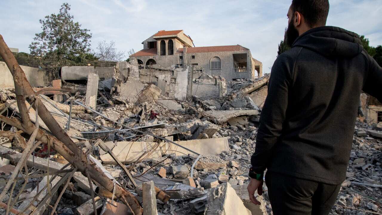 A man stands in front of homes destroyed during the conflict