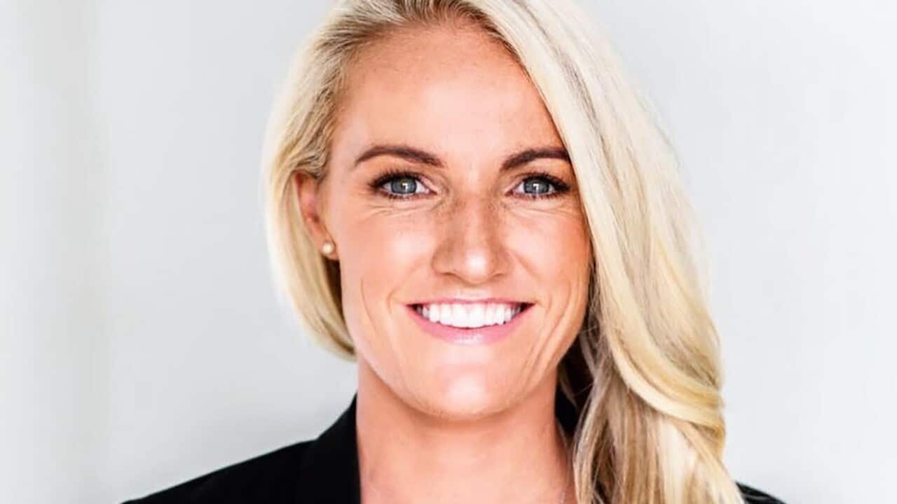 A woman with long blonde hair in a formal black outfit.