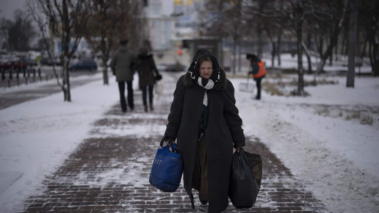A woman walks in central Kyiv, Ukraine carrying backs on a snow-covered street