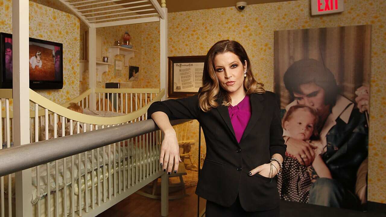 Lisa Marie Presley stands next to her crib, leaning on the exhibition
