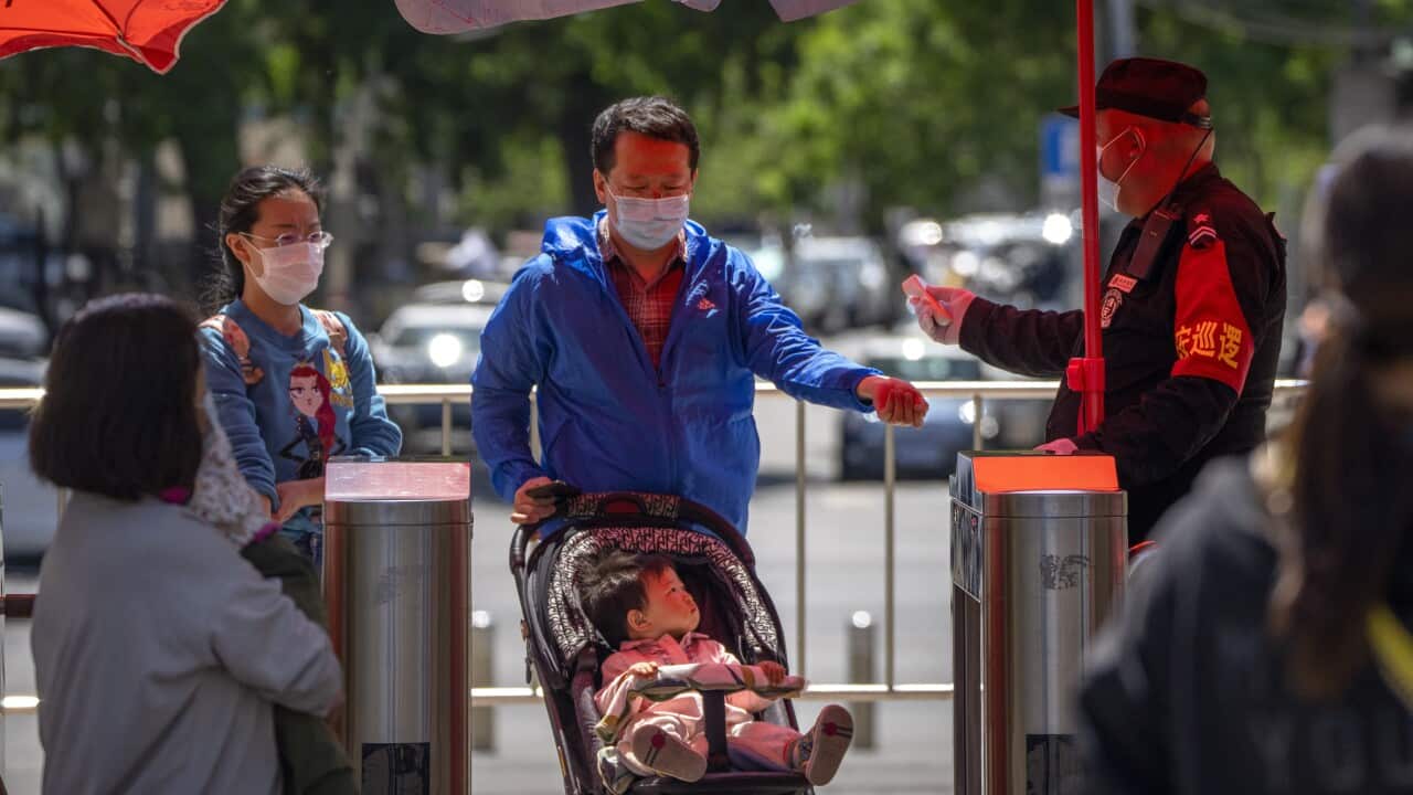 A security guard wearing a face mask takes the temperature of visitors as they enter a public park in Beijing