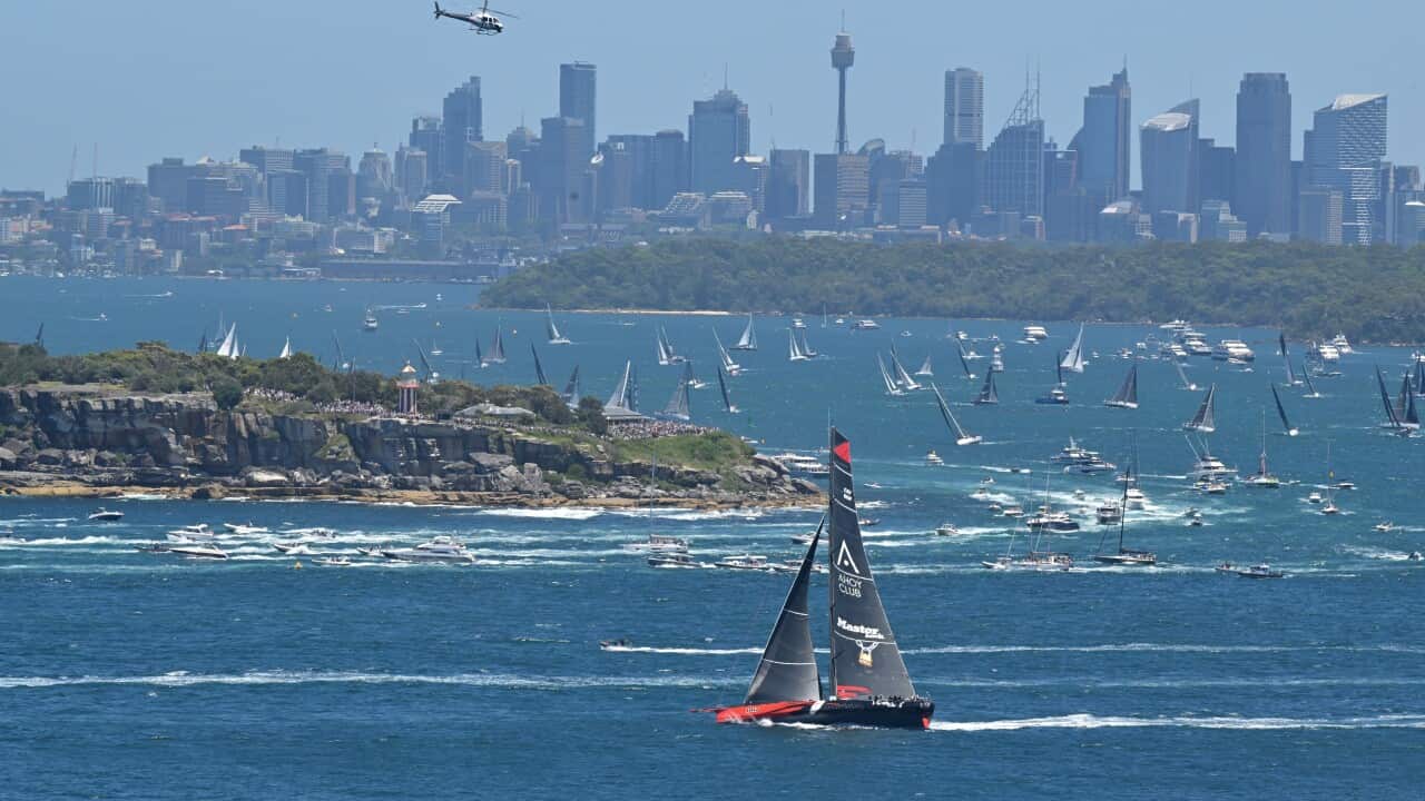 A sailing boat near a harbour with other boats seen in the background