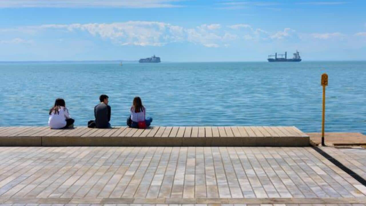 Young people enjoying summer afternoon at the pier of Thessaloniki, Greece with several ships in background