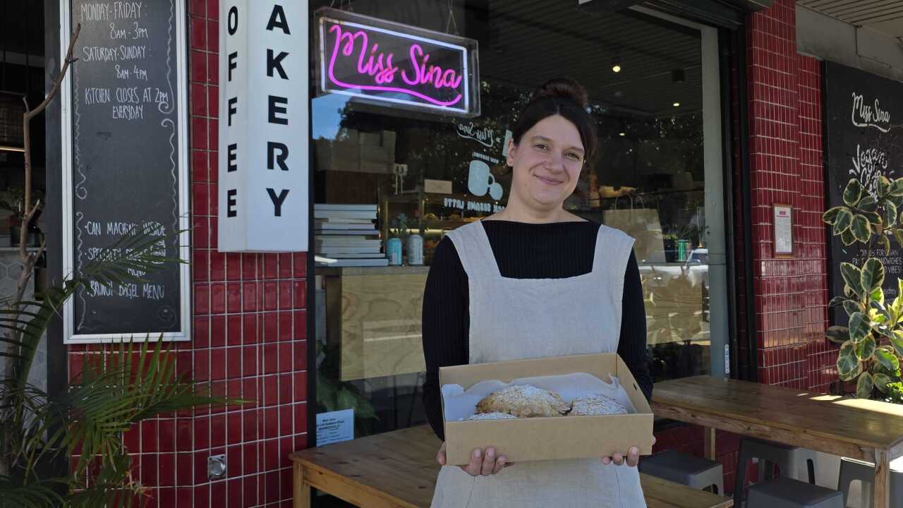 A woman standing outside a bakery holding a tray of croissants