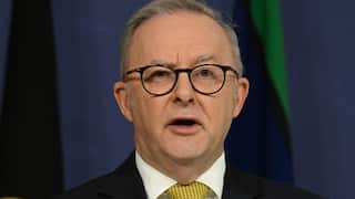 Prime Minister Anthony Albanese, in a suit, tie and glasses, is speaking to reporters.