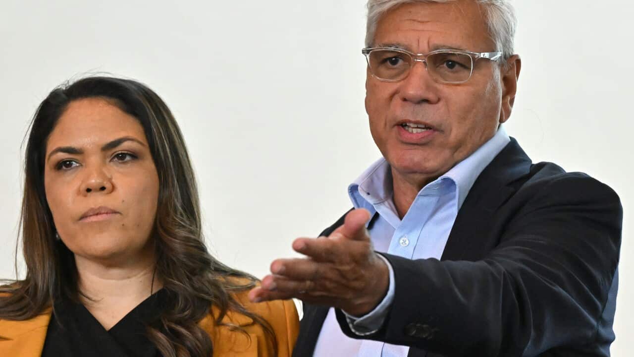 A woman and a man standing next to each other. The man is speaking and gesturing with his hand.