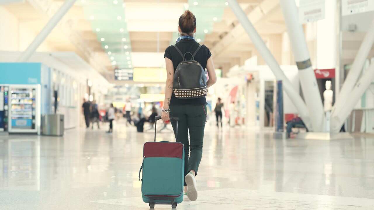 Back view of woman pulling her luggage strolling inside the airport terminal.