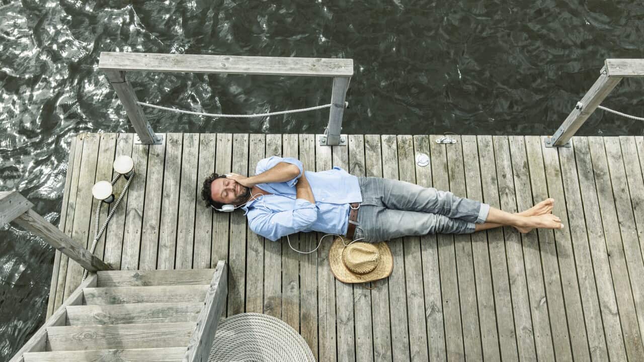 Man lying on platform at the waterside listening to music