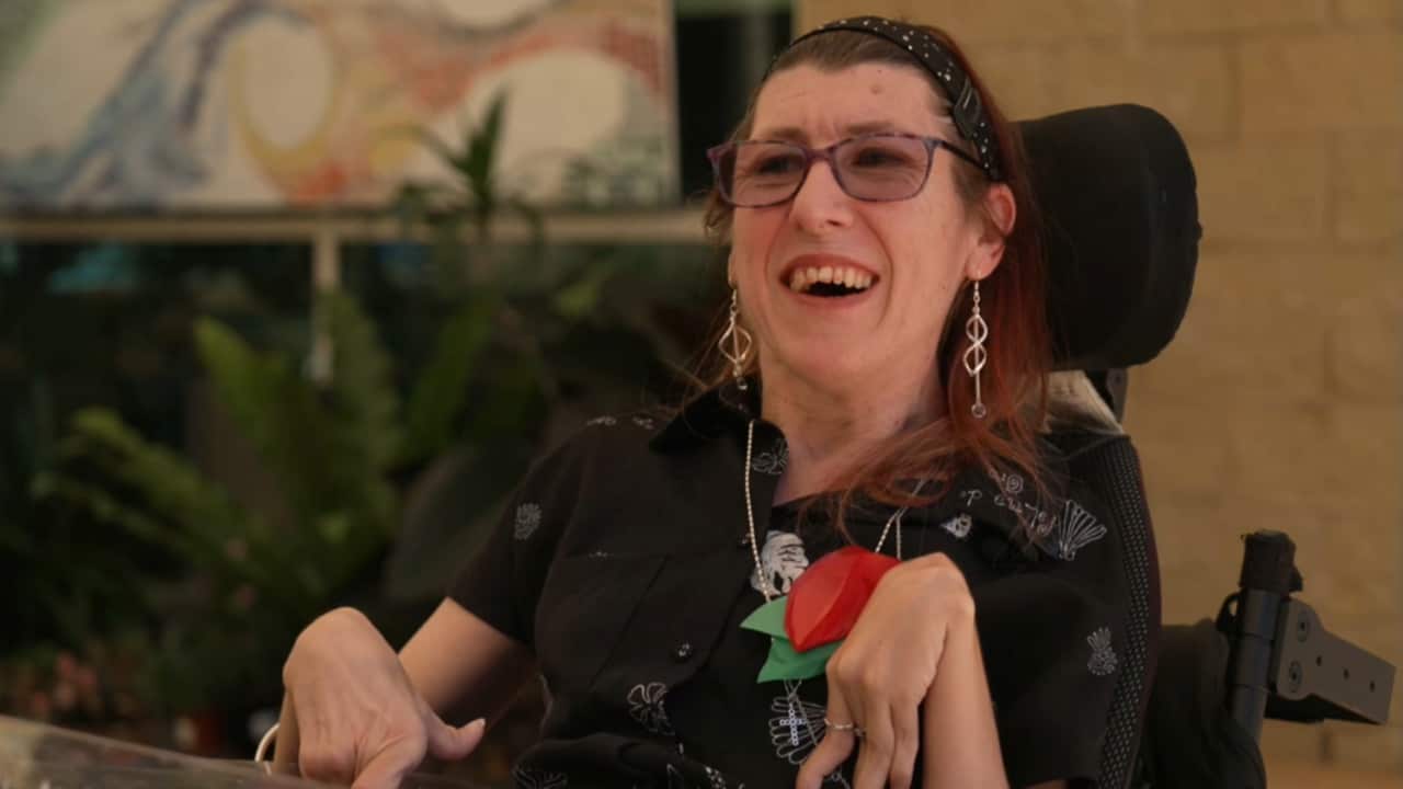 A person in a wheelchair wearing a black top and smiling.