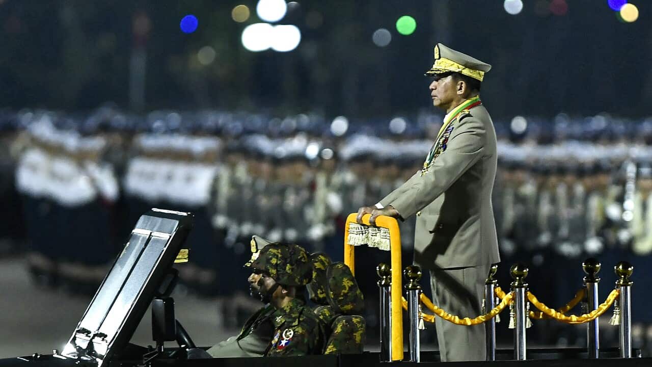 A man in formal dress stands in the back of a jeep